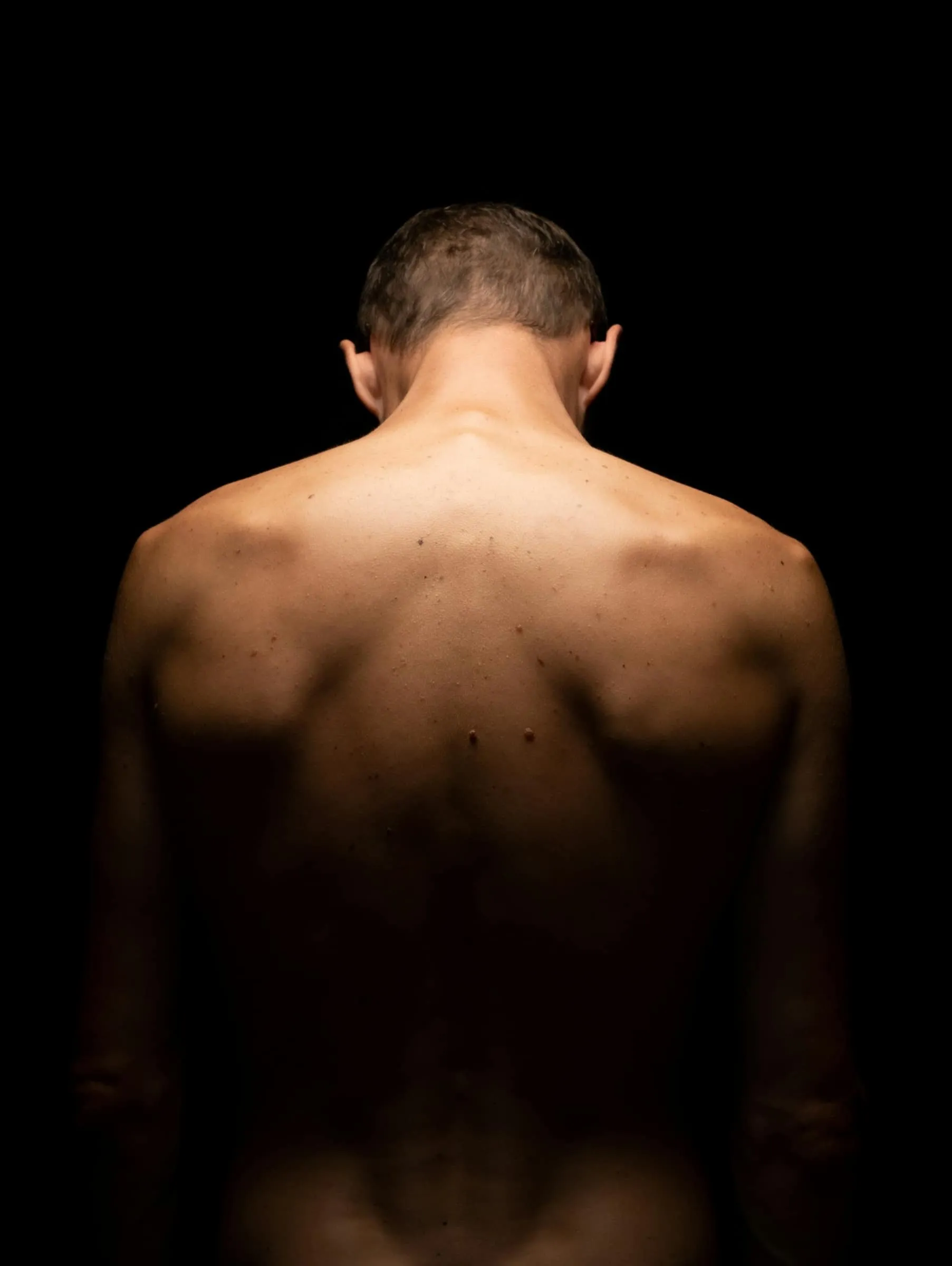 Dos nu d'un homme dans la pénombre, éclairé par une lumière chaude