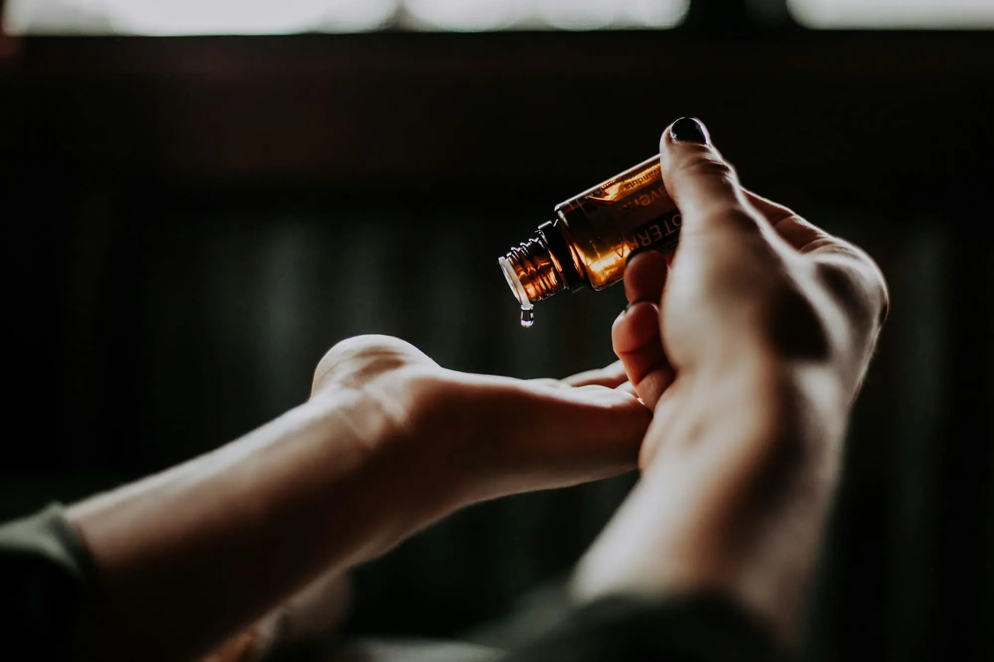 Huile de massage versée d'un flacon ambré dans la paume