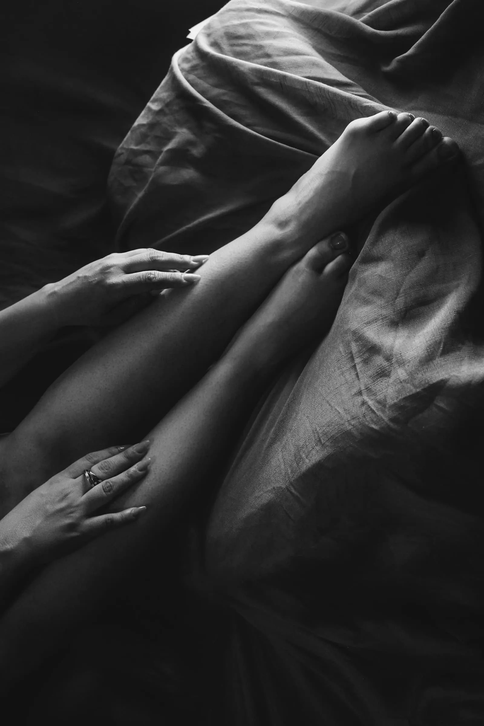 Mains posées sur des jambes enlacées dans des draps, en noir et blanc